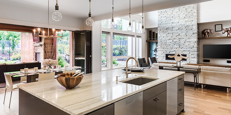 Modern open-plan kitchen and living area with marble island, pendant lights, and sliding doors to a patio.