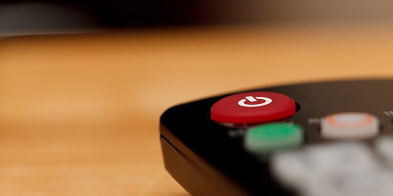 Close-up of a TV remote with a prominent red power button on a wood surface.