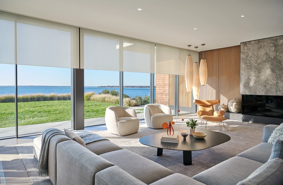 A living room with a view of the water. Lutron motorized shades are partially lowered over the windows.